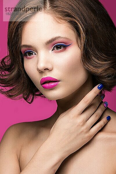 Schönes Modell Mädchen mit hellen Make-up und farbigen Nagellack. Schönes Gesicht. Kurze bunte Nägel. Bild im Studio auf einem rosa Hintergrund genommen