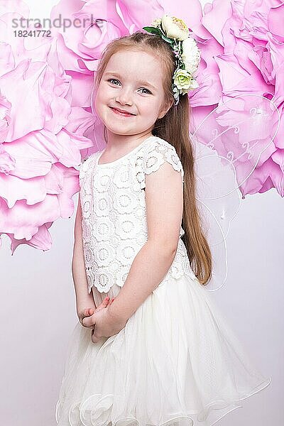 Kleines Feenmädchen im weißen Kleid auf einem Hintergrund aus Blumen. Foto im Studio aufgenommen