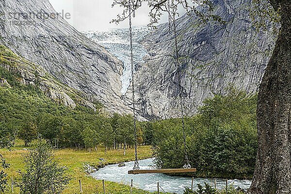 Eine Schaukel häng mit Blick auf den Gletscher Briksdalsbreen in Norwegen an einem Baum