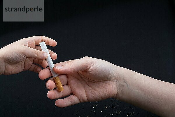 Hand gibt Zigarette auf einem schwarzen Hintergrund aus
