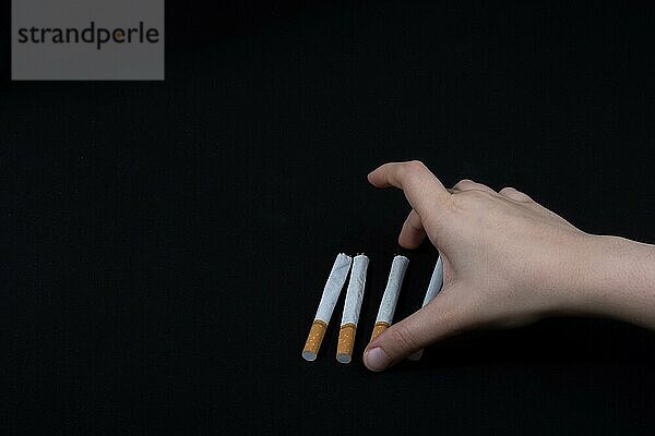 Hand hält eine Zigarette auf schwarzem Hintergrund