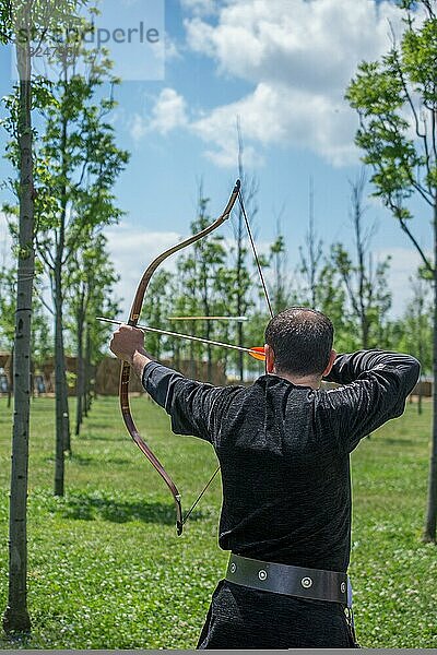 Bogenschütze mit Bogen in traditioneller Kleidung schießt einen Pfeil