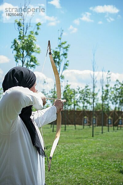 Bogenschütze mit Bogen in traditioneller Kleidung schießt einen Pfeil