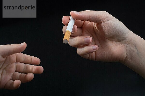 Hand gibt Zigarette auf einem schwarzen Hintergrund aus