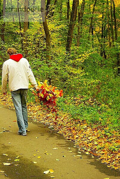 Junger Mann mit Blättern in der Hand bei einem Herbstspaziergang im Wald