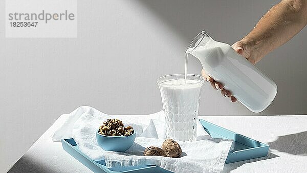 Person gießt Milch voll Glas mit Walnüssen Tablett  Auflösung und hohe Qualität schönes Foto