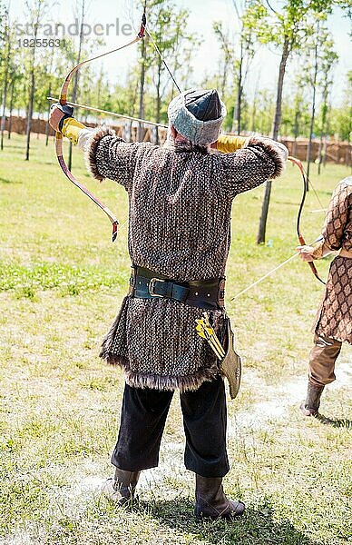 Bogenschütze mit Bogen in traditioneller Kleidung schießt einen Pfeil