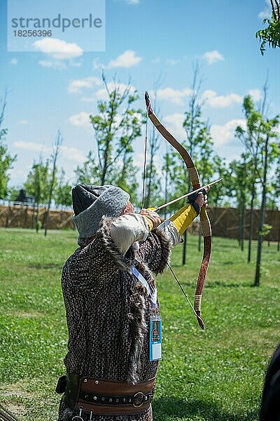 Bogenschütze mit Bogen in traditioneller Kleidung schießt einen Pfeil