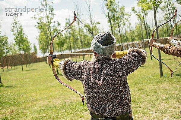 Bogenschütze mit Bogen in traditioneller Kleidung schießt einen Pfeil