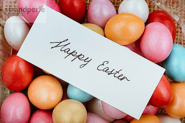 Frohe Ostern geschrieben auf einem kleinen Stück Papier auf bunten dekorativen Steinen in der Auslage