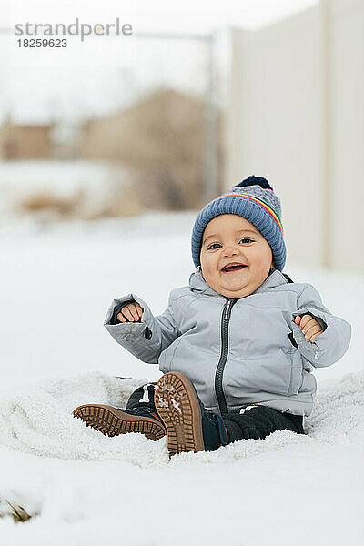 Glücklicher kleiner Junge  der draußen in Schneeanzug und Mütze im Schnee spielt