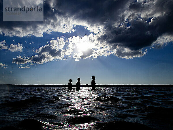 Silhouette von Teenagern im See mit Sonnenstrahlen und Wolken