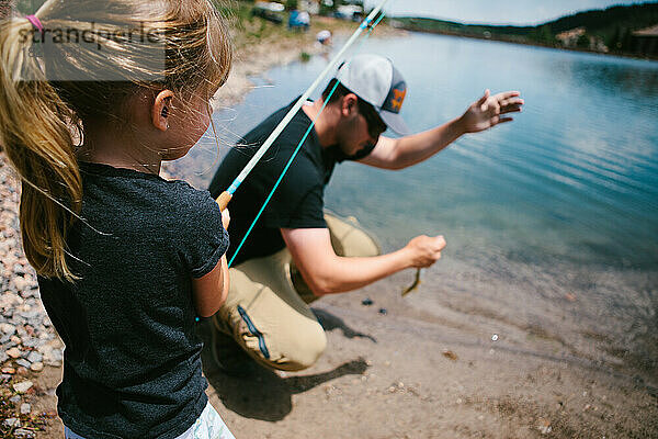 Mädchen fängt Fische mit Hilfe des Vaters am Seeufer des Bergsees