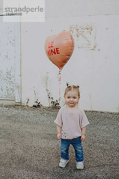 Glückliches Kleinkind  das draußen mit Herz-Valentinstag-Ballon steht