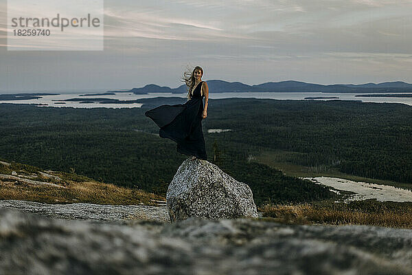 Schöne junge Frau und langes Kleid balancieren auf einem Felsen auf dem Berggipfel