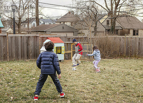Ein Vater spielt Fußball mit Kindern im Hof ??neben dem Hühnerstall