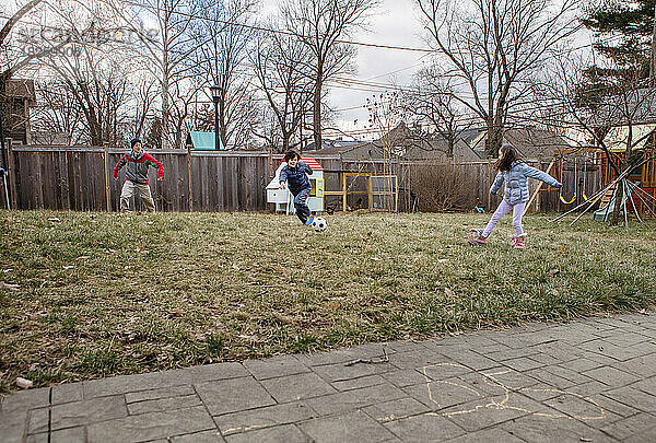 Ein Junge spielt im Winter mit seiner Familie im Hinterhof eines Vorortes Fußball