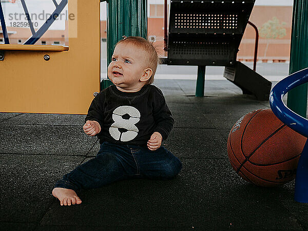 Baby spielt draußen im Klettergerüst der Schule und sitzt neben einem Korb