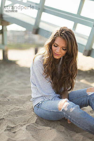 Schöne junge Frau sitzt allein am Strand in Kalifornien