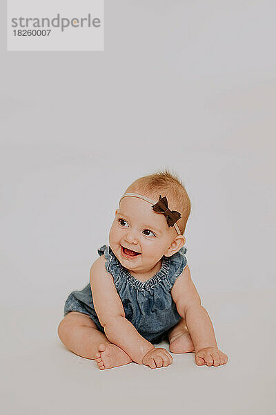 Lächelndes  glückliches Baby im Jeanskleid und einer Schleife auf dem Kopf