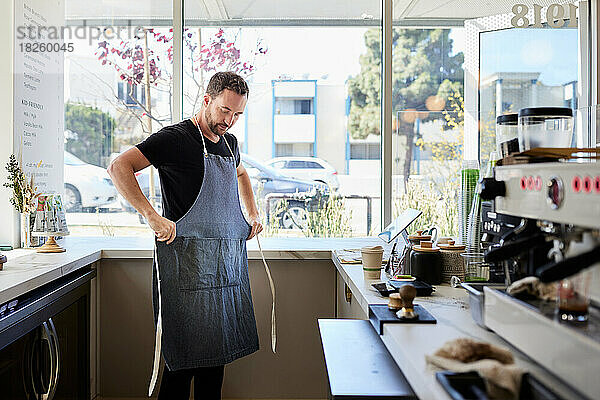 Männlicher Unternehmer trägt Schürze in der Küche eines Cafés