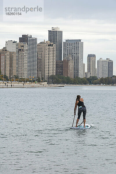 Rückansicht einer Frau beim Paddeln im See mit der Stadt im Hintergrund