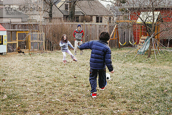 Zwei Kinder spielen mit Vater im Hof ??mit Hühnern Fußball