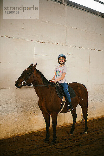 Glückliches Mädchen auf braunem Pony für Reitunterricht in der Scheune