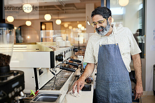 Lächelnder reifer männlicher Unternehmer putzt Küchentheke im Café