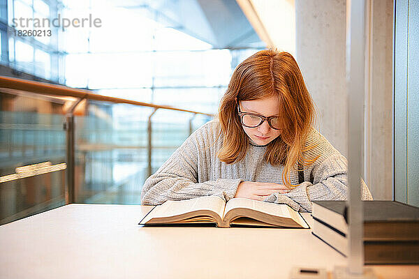 Teenager-Mädchen mit roten Haaren und Brille lernt in der Stadtbibliothek.