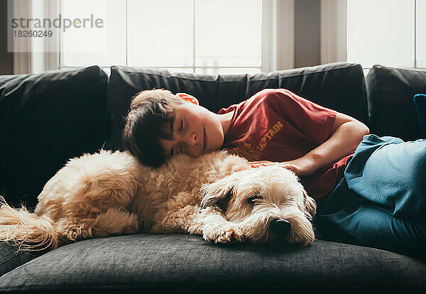 Netter glücklicher Junge und flauschiger Hund liegen zusammen auf dem Sofa.