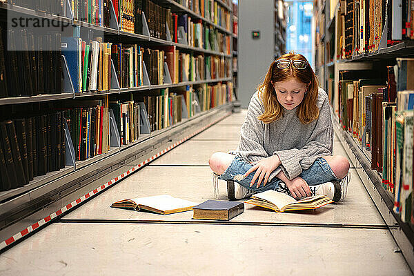 Teenager-Mädchen mit roten Haaren und Brille lernt in der Bibliothek.
