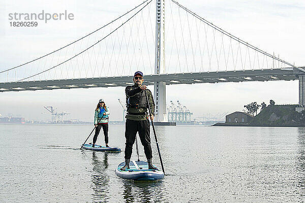 Freunde paddeln  während die Oakland Bay Bridge im Hintergrund zu sehen ist