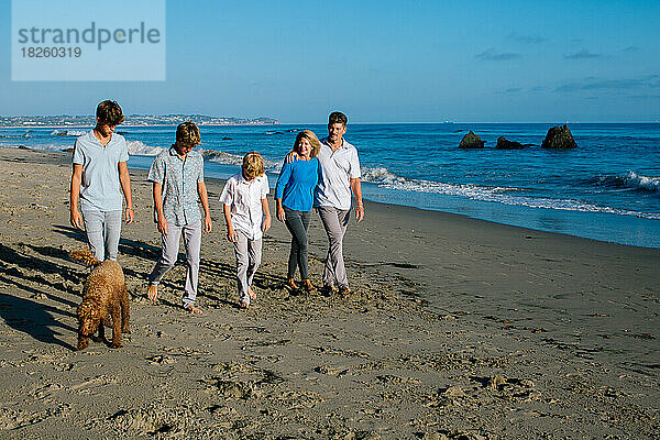 Fünfköpfige Familie und Hund spazieren entlang der Küste von Malibu