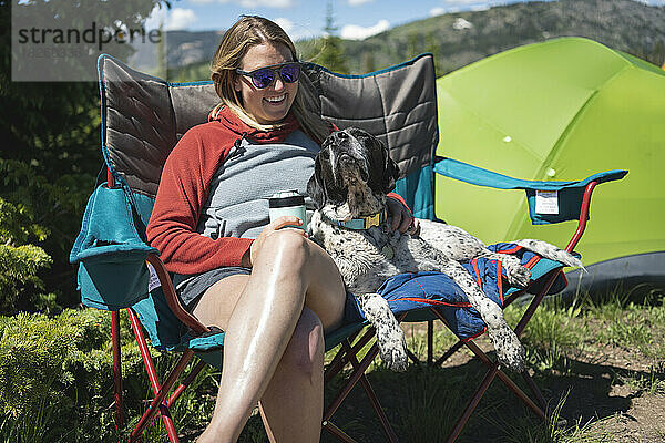 Glückliche Frau  die an einem sonnigen Tag mit Hund in Campingstühlen sitzt