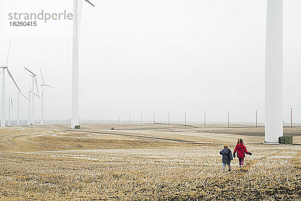 Zwei Kinder gehen auf eine Reihe riesiger Windmühlen zu