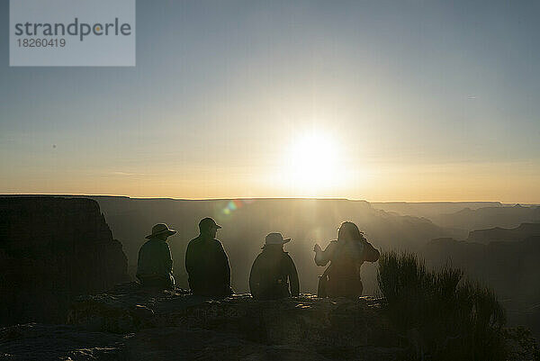 Eine Gruppe von vier Personen sitzt auf dem Felsvorsprung des Canyons  der vom Sonnenuntergang beleuchtet wird