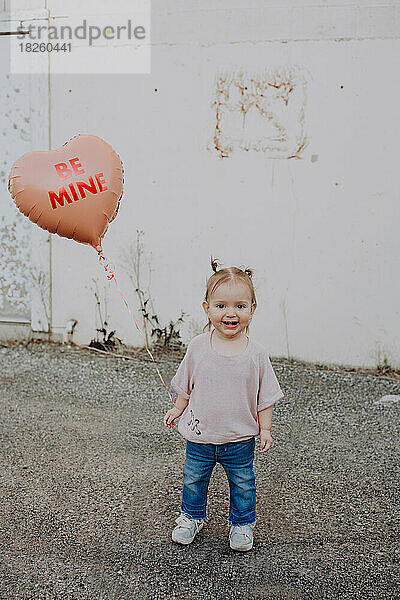 Glückliches Kleinkind  das draußen mit einem Herz-Valentinsballon steht