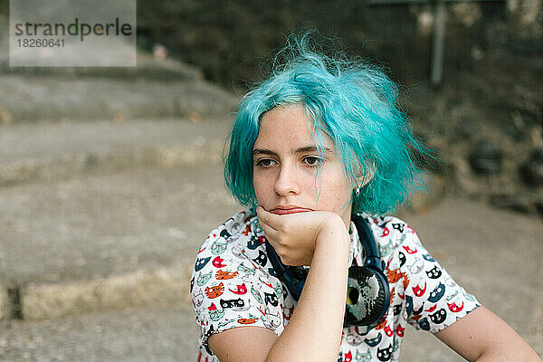 Teenager-Mädchen mit blauen Haaren sitzt mit ihrem Gesicht in der Hand