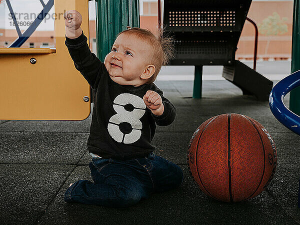 Baby spielt draußen im Klettergerüst der Schule und sitzt neben einem Korb