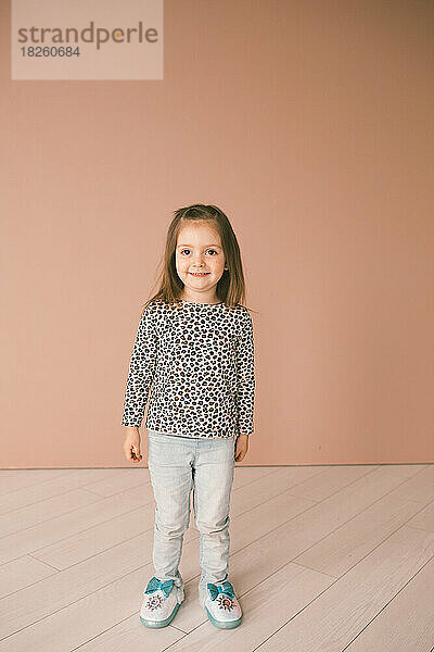 Kleines Mädchen lächelt vor einer rosa Wand und trägt ein Gepardenhemd