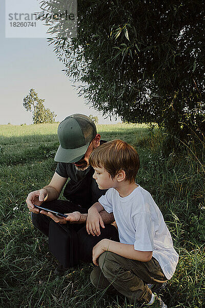 Vater und Sohn im Park und schauen aufs Handy