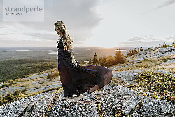 Wind bläst Frau mit langen Haaren und Kleid bei Sonnenuntergang auf dem Berg