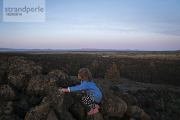 Ein junges Mädchen klettert in der Abenddämmerung auf Felsen mit Blick auf eine weite Wüste