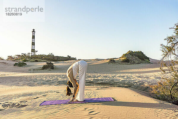 Eine Frau praktiziert Yoga auf einer Matte in einer atemberaubenden Düne in der Nähe eines Leuchtturms