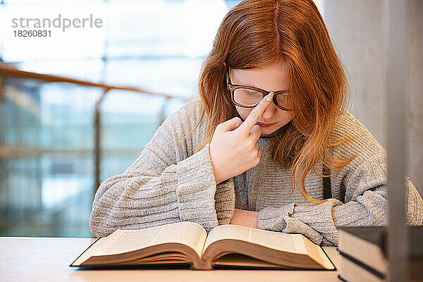 Teenager-Mädchen mit roten Haaren lernt in der Stadtbibliothek.