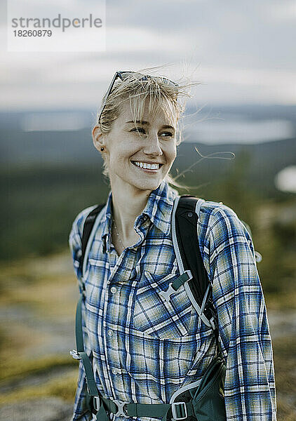 Blonde junge Frau im Flanellhemd lächelt beim Wandern in Maine