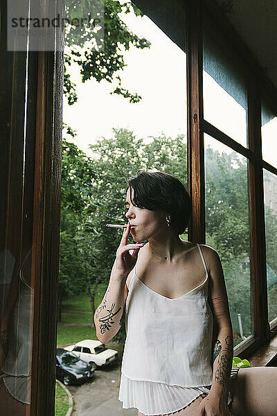 Frau mit Tätowierungen raucht  während sie auf dem Balkon steht