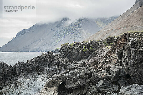 Ein Mann geht auf Felsen über dem Meer an der Südküste Islands.
