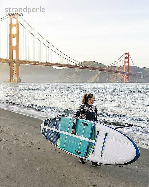 Frau mit Paddleboard läuft in Richtung Golden Gate Bridge